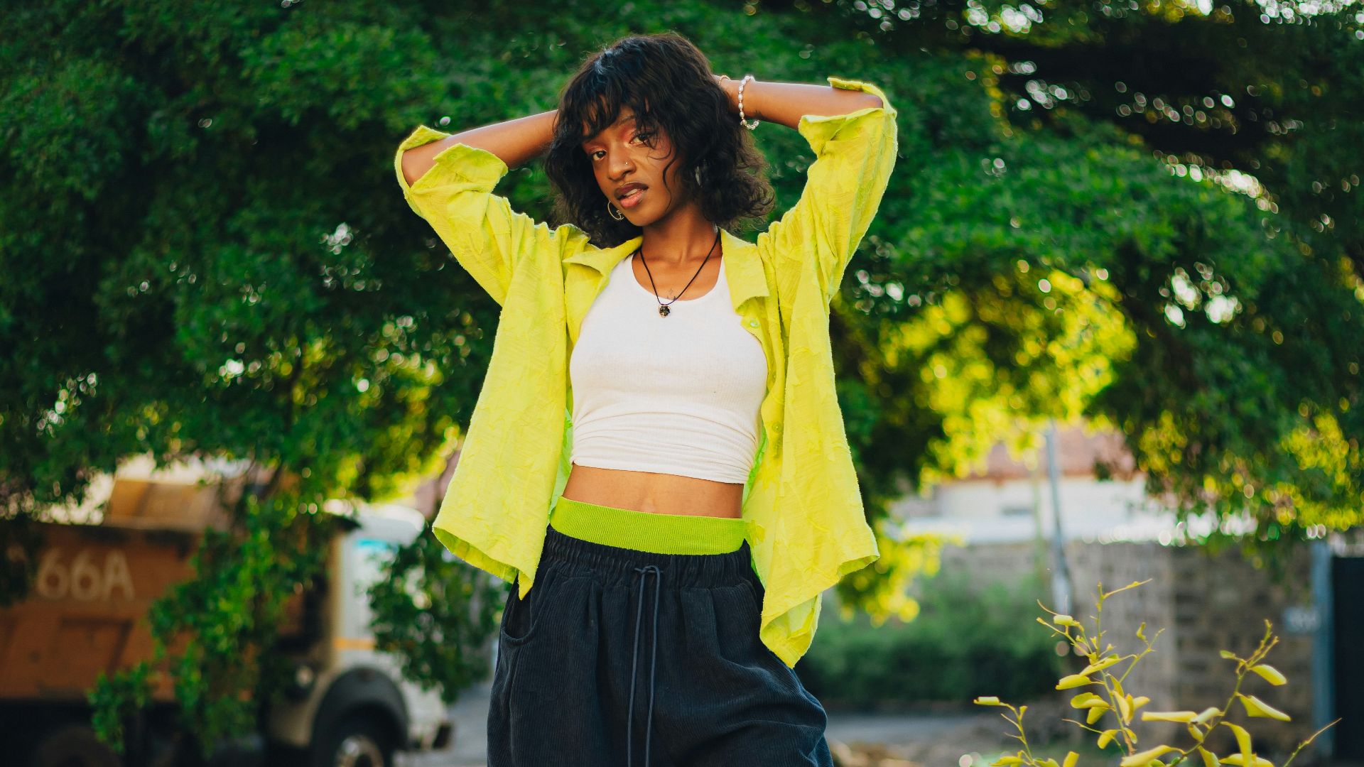 Woman standing outdoors with hands behind head.