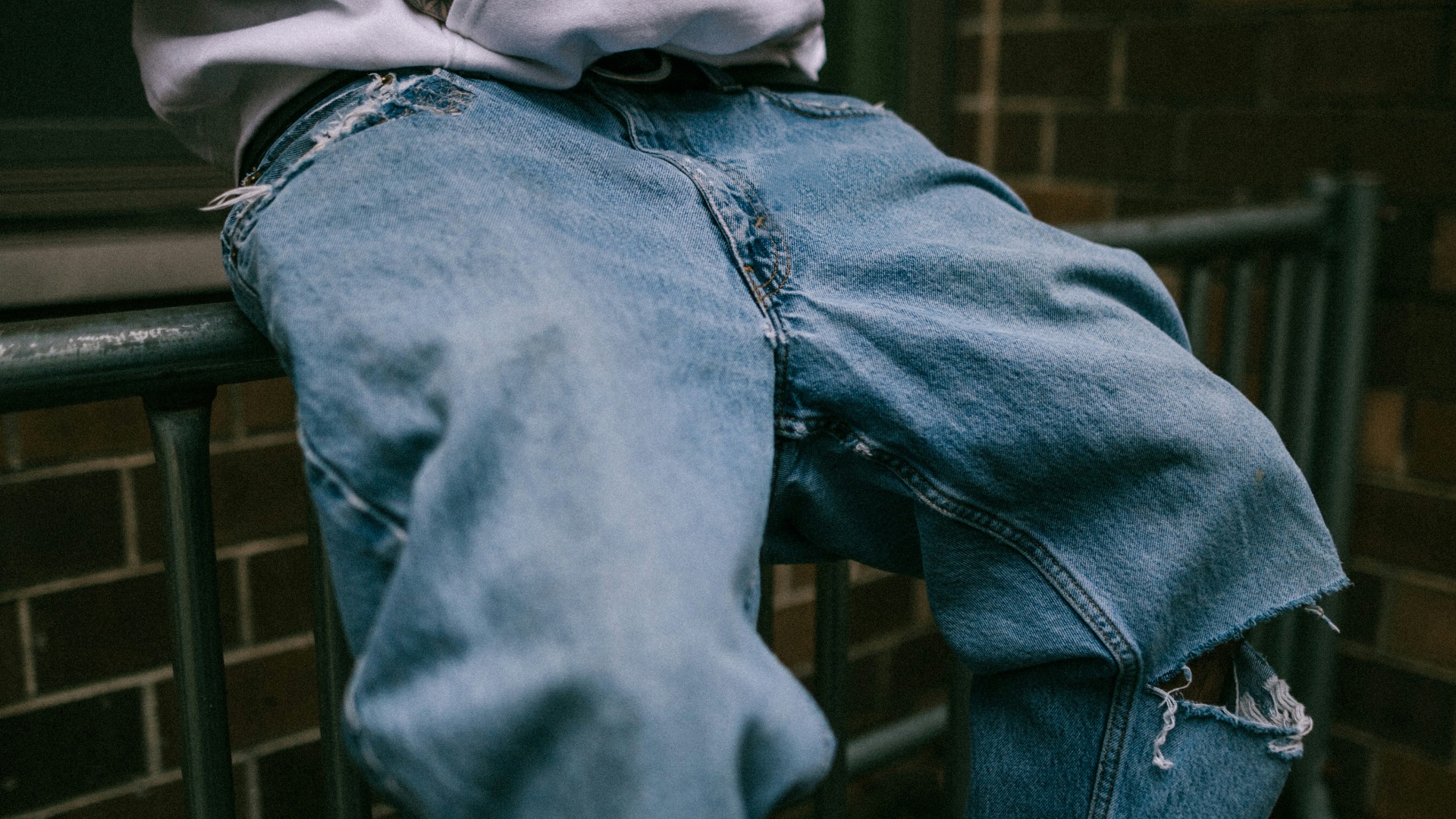 a man sitting on a rail wearing a white hoodie and blue jeans