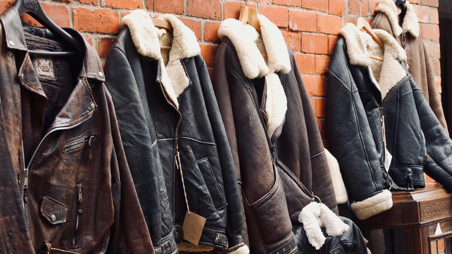 four assorted leather jackets hanging on brown brick wall