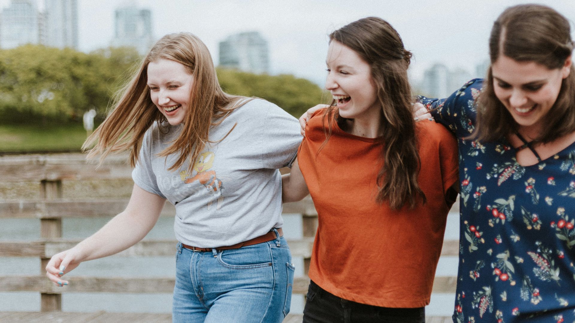 three women walking on brown wooden dock near high rise building during daytime