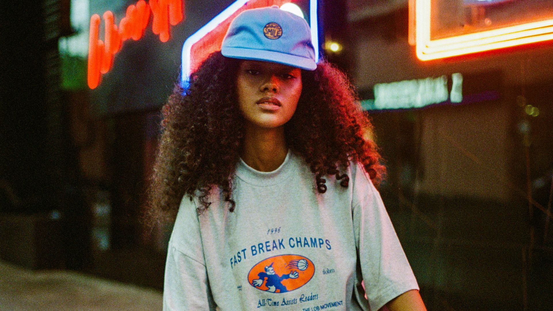A woman sitting on the ground in front of a neon sign