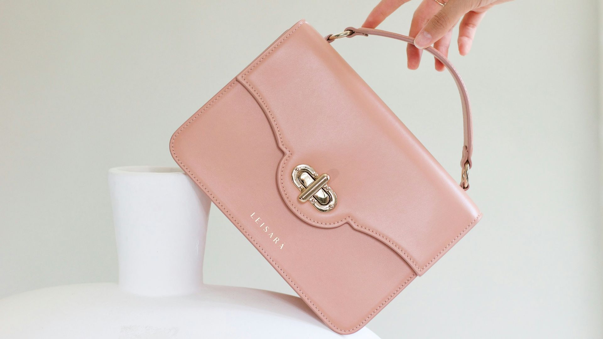 a woman holding a pink purse over a white vase