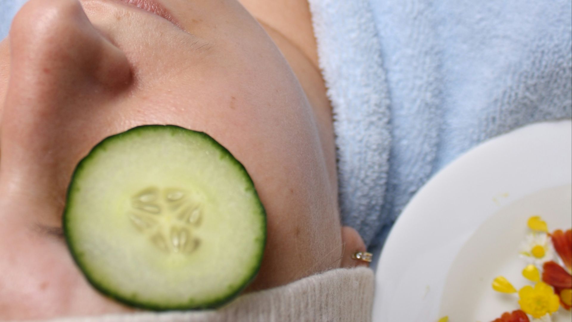 woman wearing blue robe lying with cucumber on eye