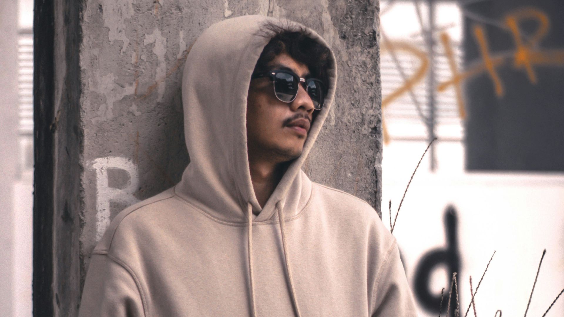 men wearing a grey hoodie jacket leaning in a wall during daytime