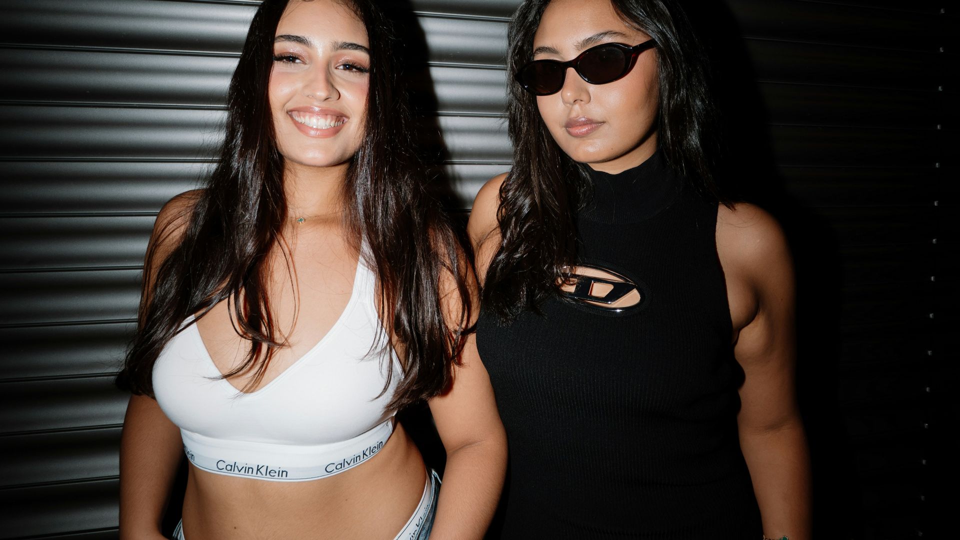 Two young women posing in front of a dark wall