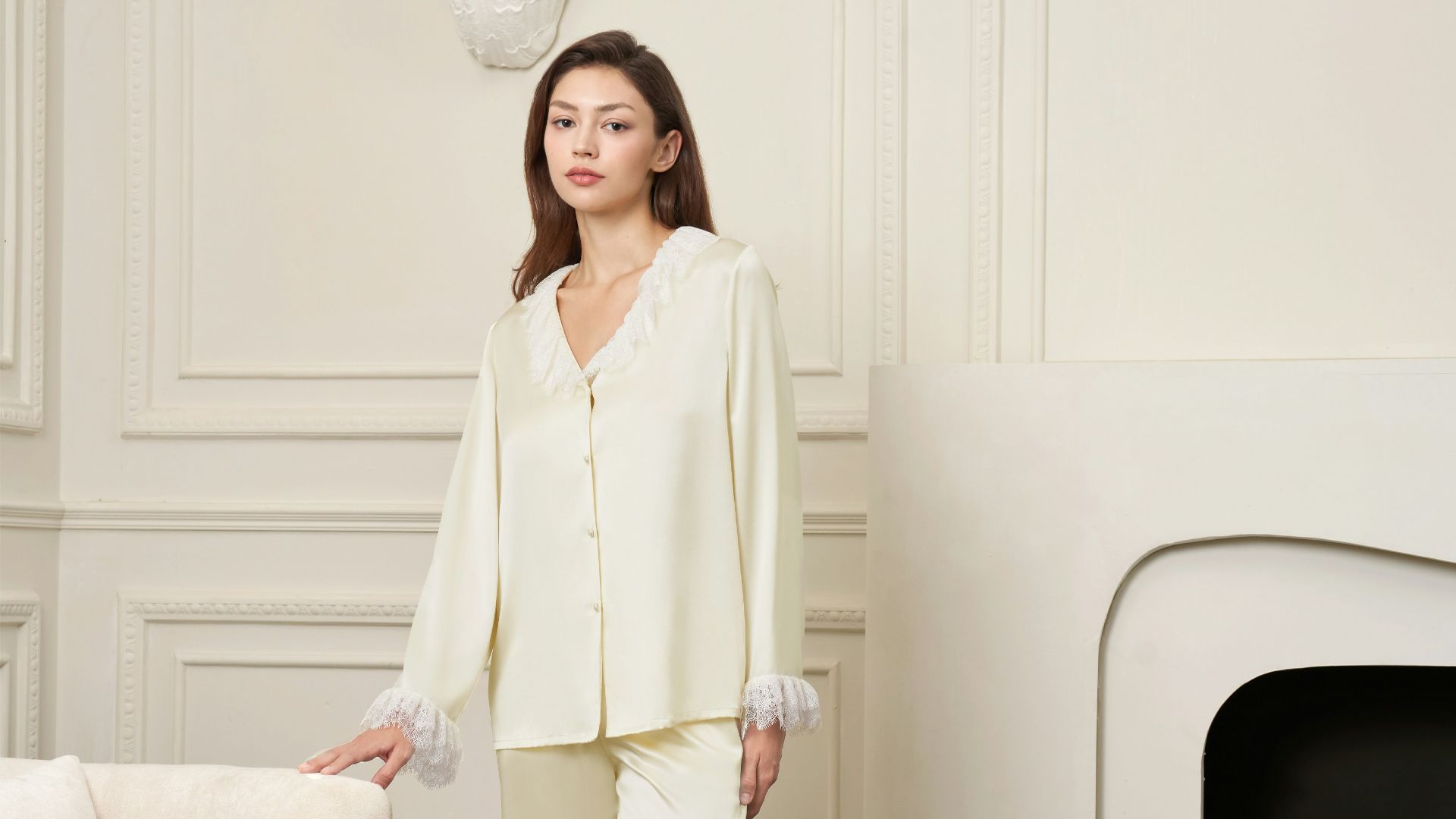 A woman in silk pajamas stands in a room.