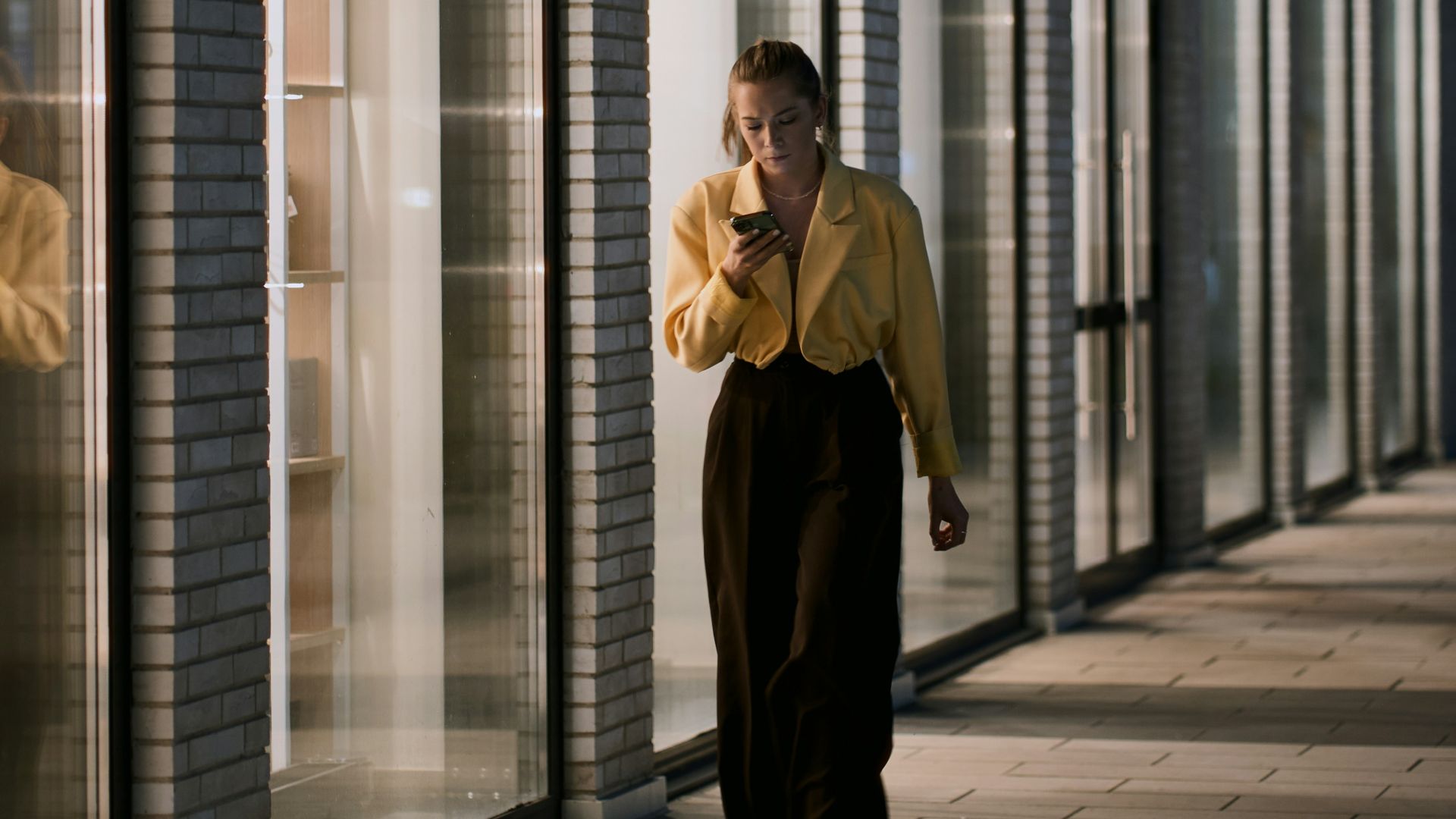 Woman walking at night with phone near building
