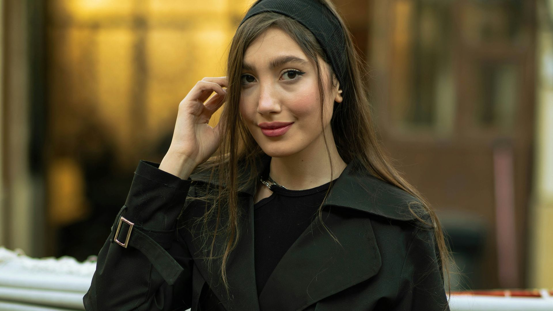 A young woman in a black trench coat smiles.