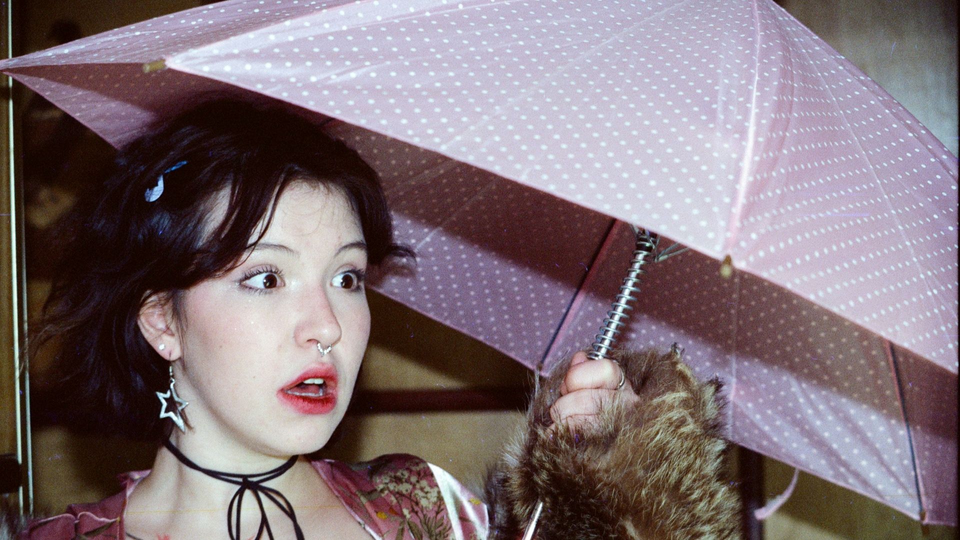 Woman holding a pink polka dot umbrella with raccoon.