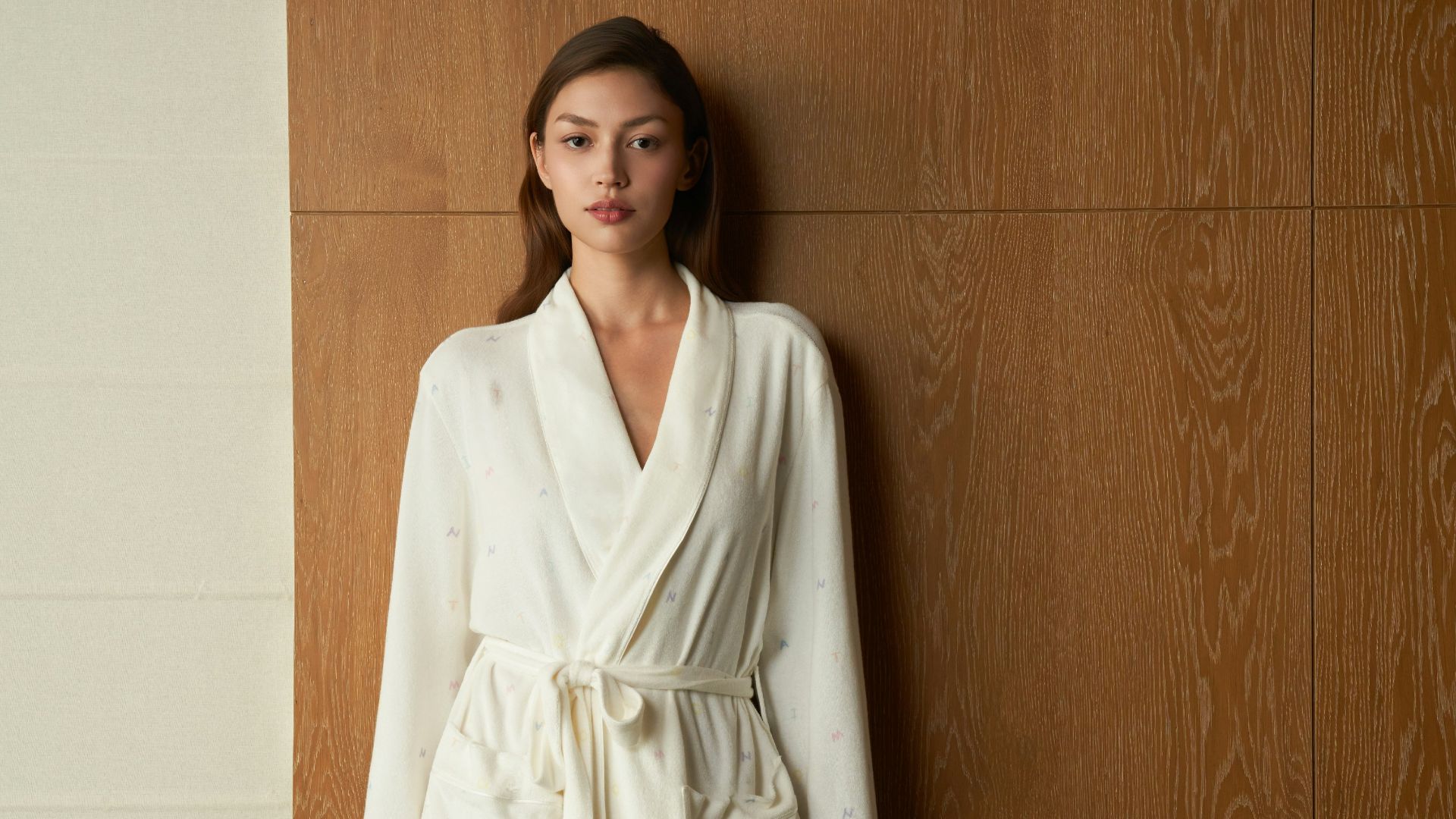 Woman wearing a white bathrobe standing against wooden wall