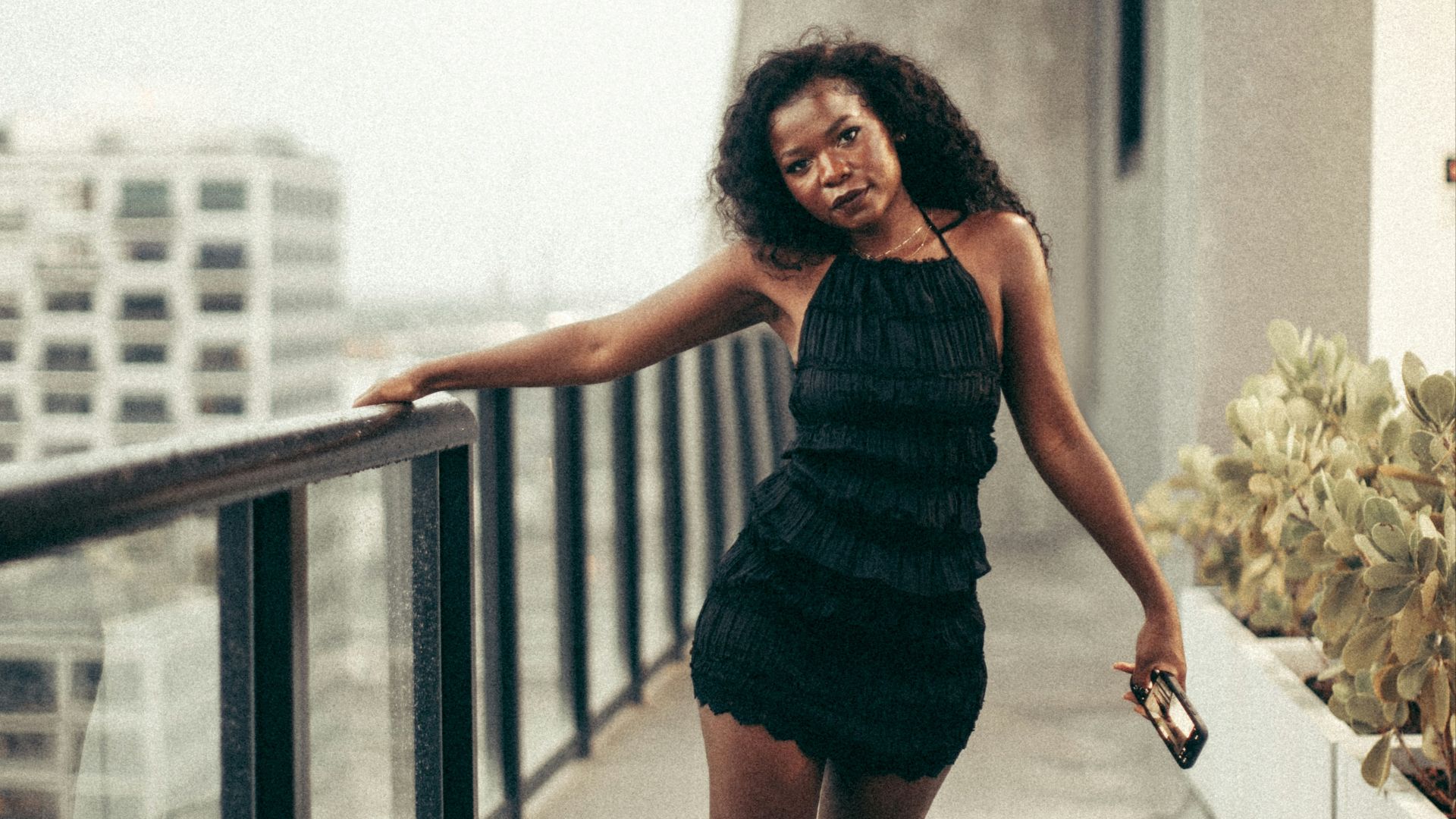 Woman poses on a balcony overlooking a cityscape.