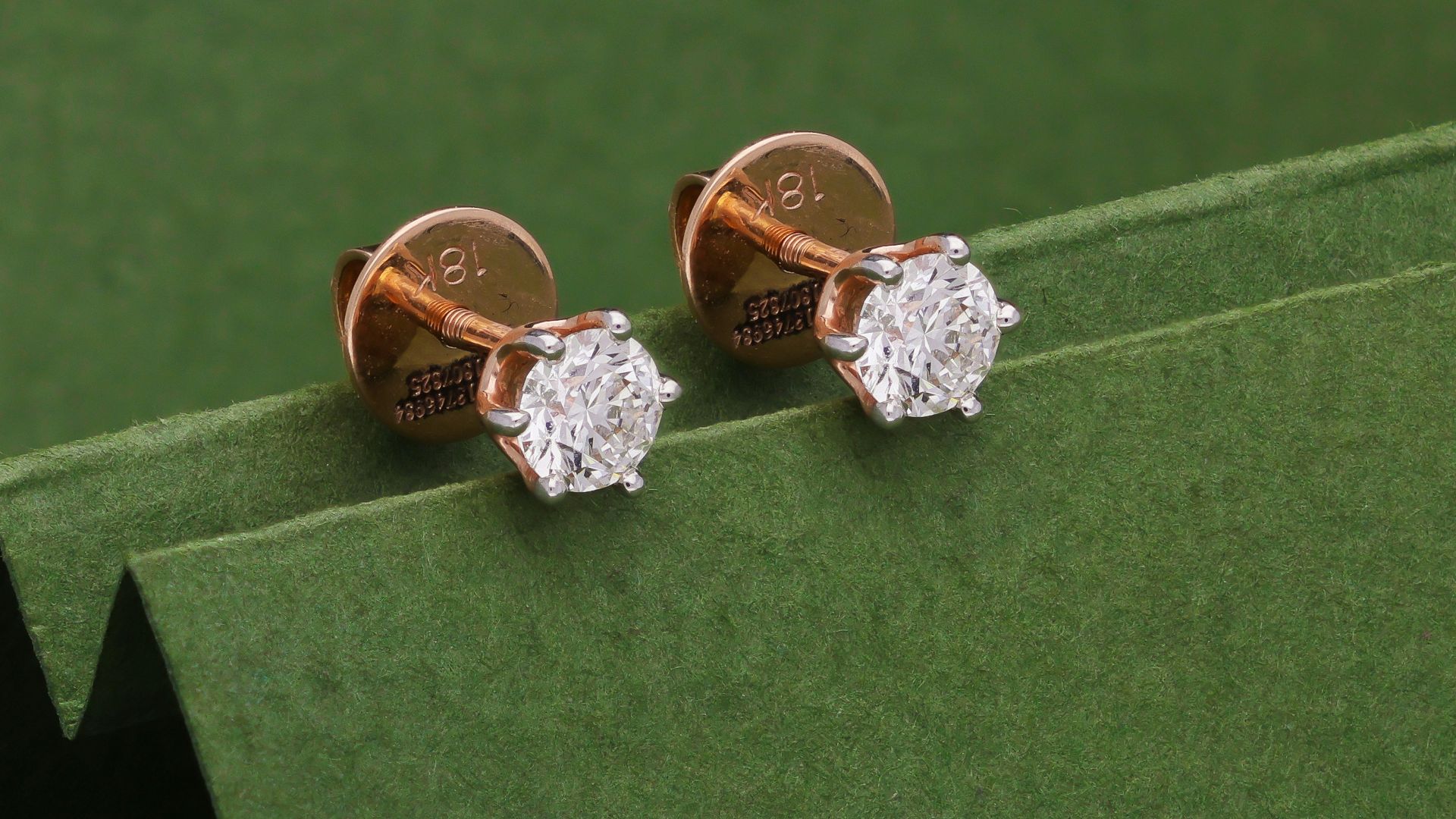 Two small diamond stud earrings on green background