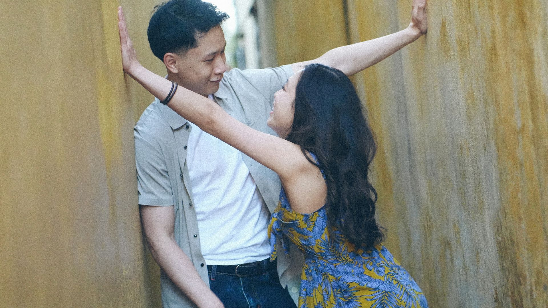 Couple leaning against a textured yellow wall