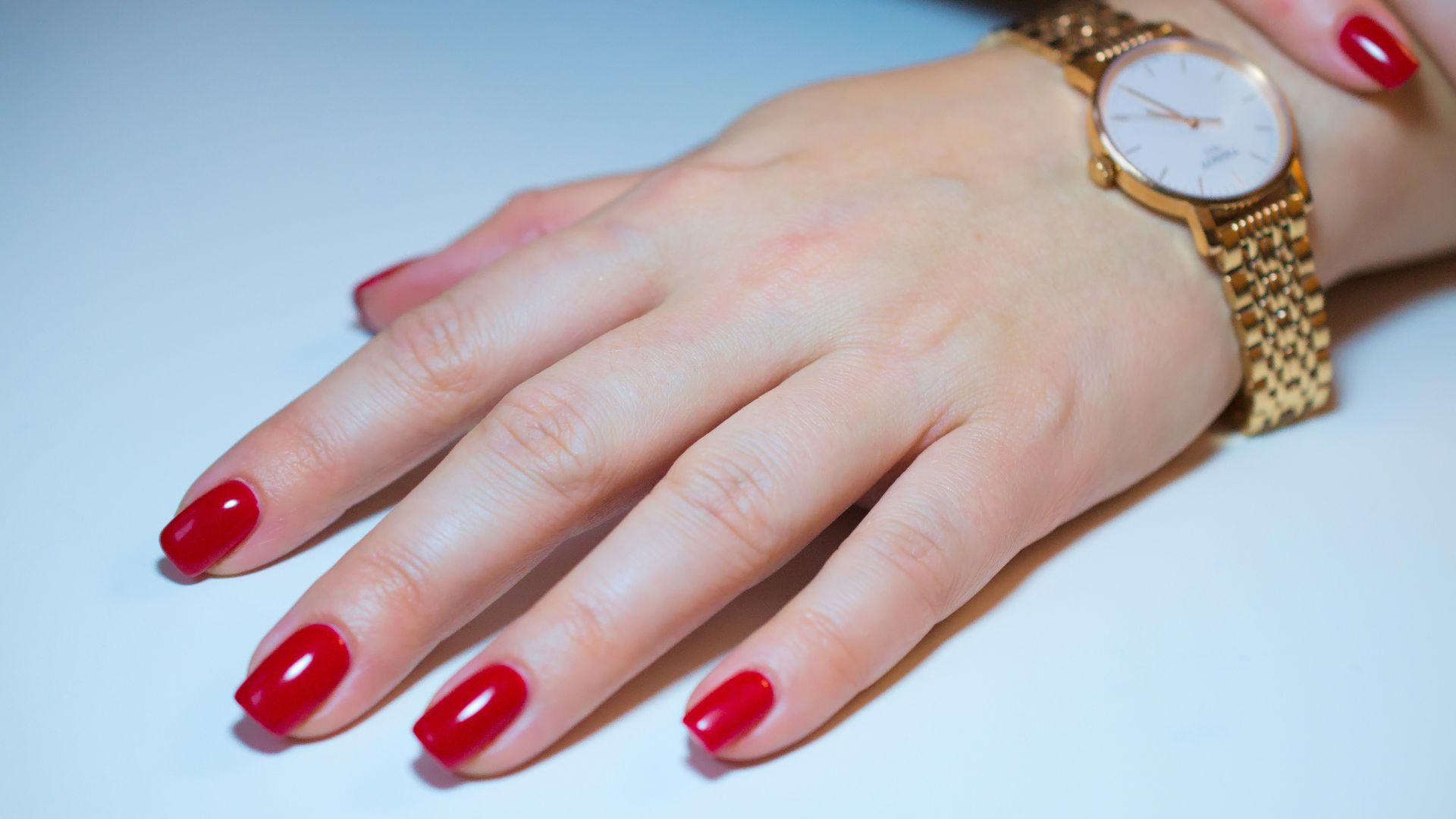 a woman's hand with red fingernails and a gold watch