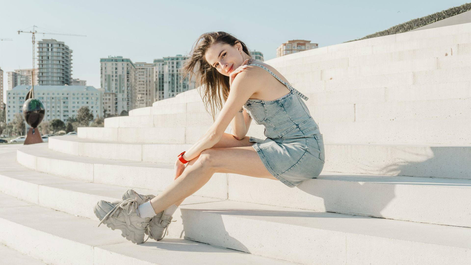 Young woman in denim dress sitting on white steps
