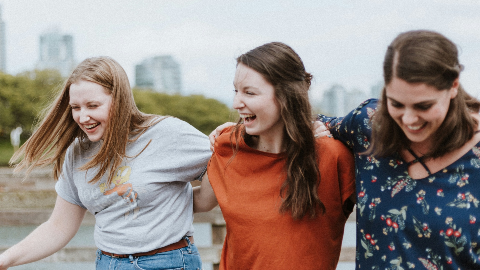 three women walking on brown wooden dock near high rise building during daytime