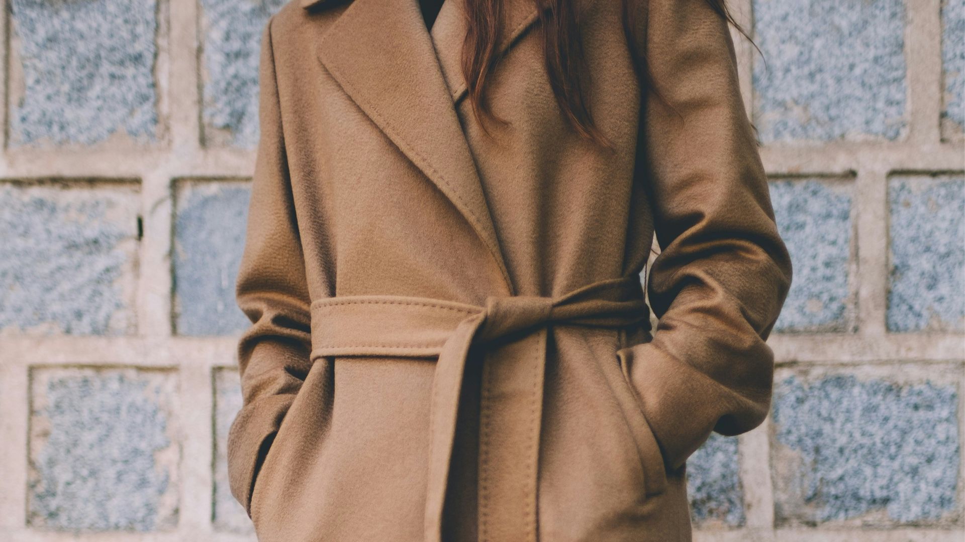 woman wearing brown single-breasted coat standing in front of gray brick wall