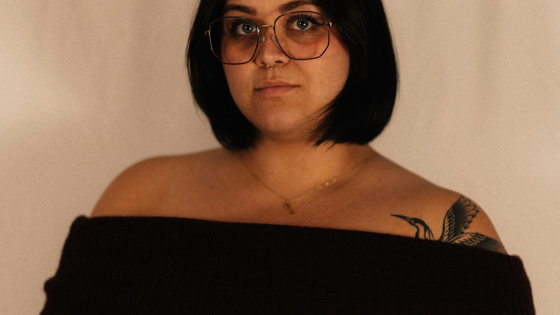 Woman with dark hair and glasses wearing off-shoulder top.