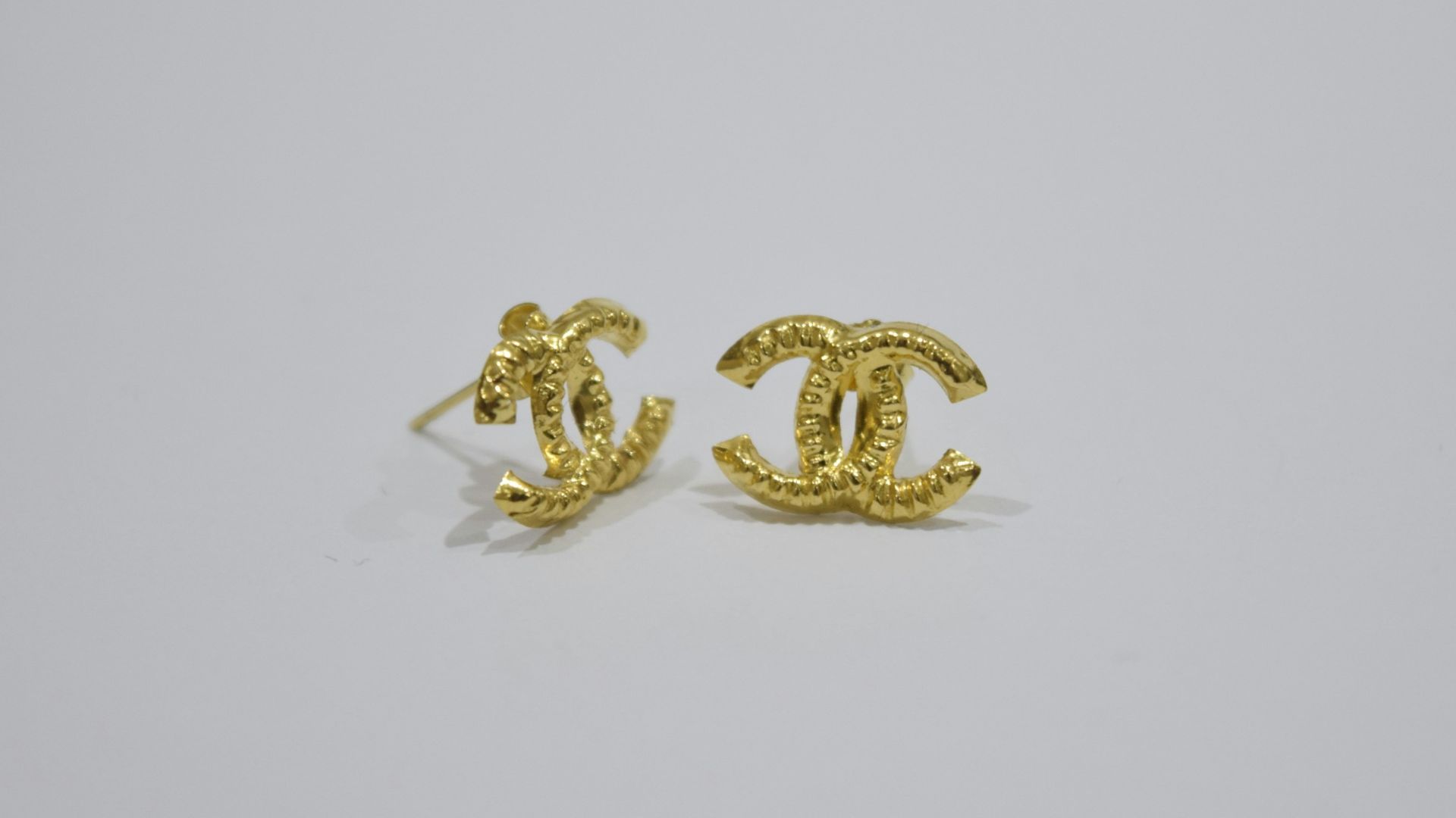 Gold interlocking cc logo earrings on white background