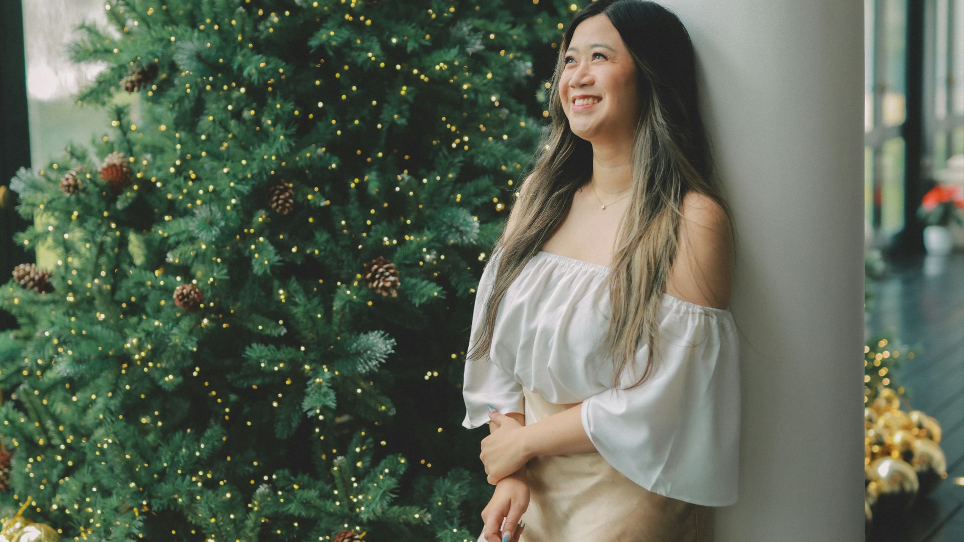 A woman smiles near a decorated christmas tree.