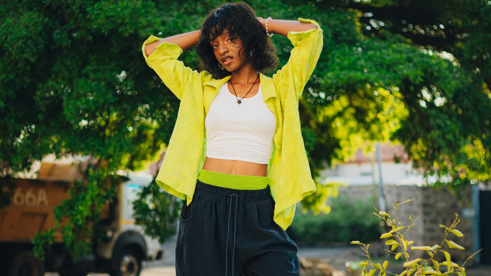 Woman standing outdoors with hands behind head.