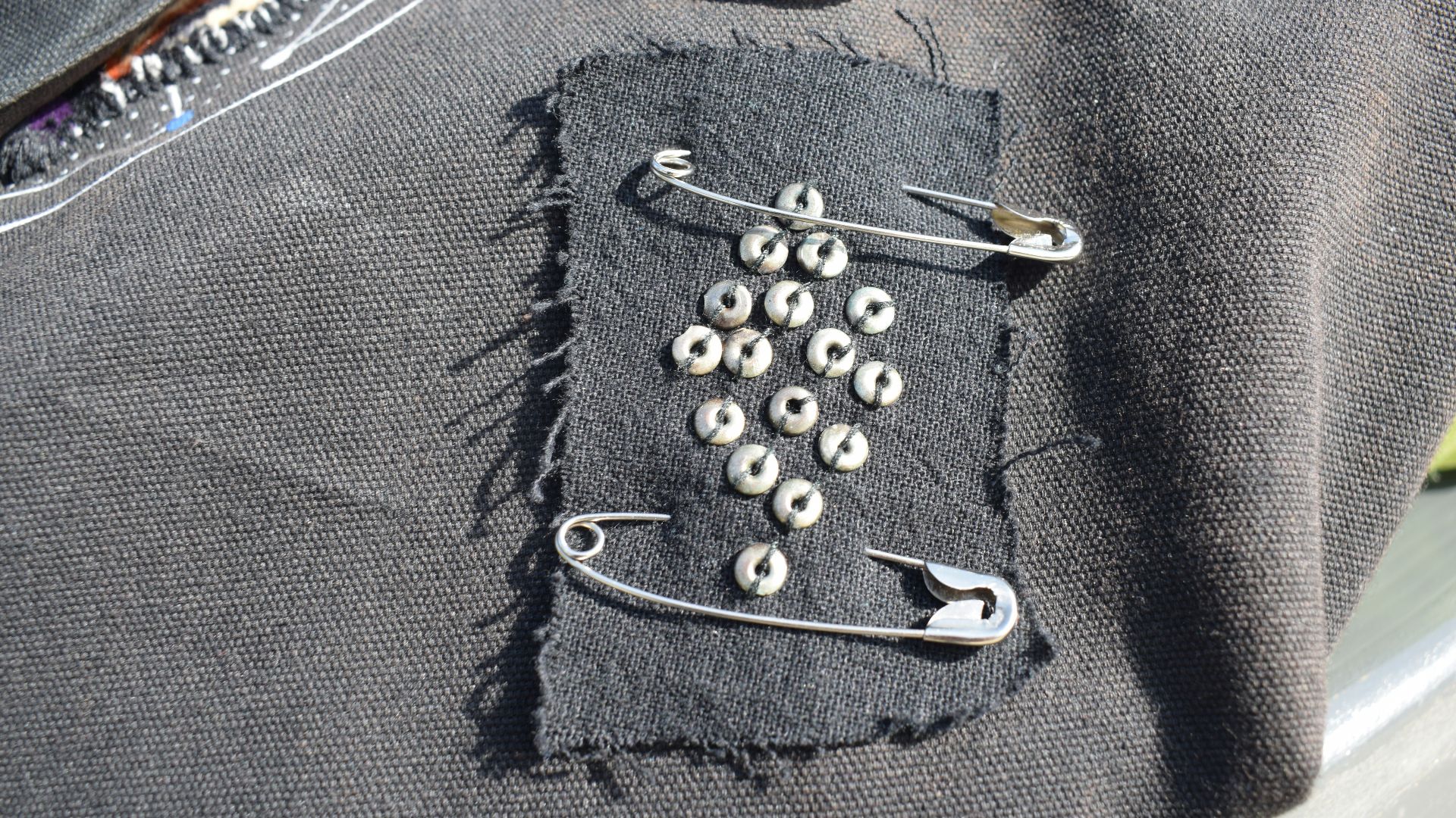Black fabric patch with safety pins and studs.