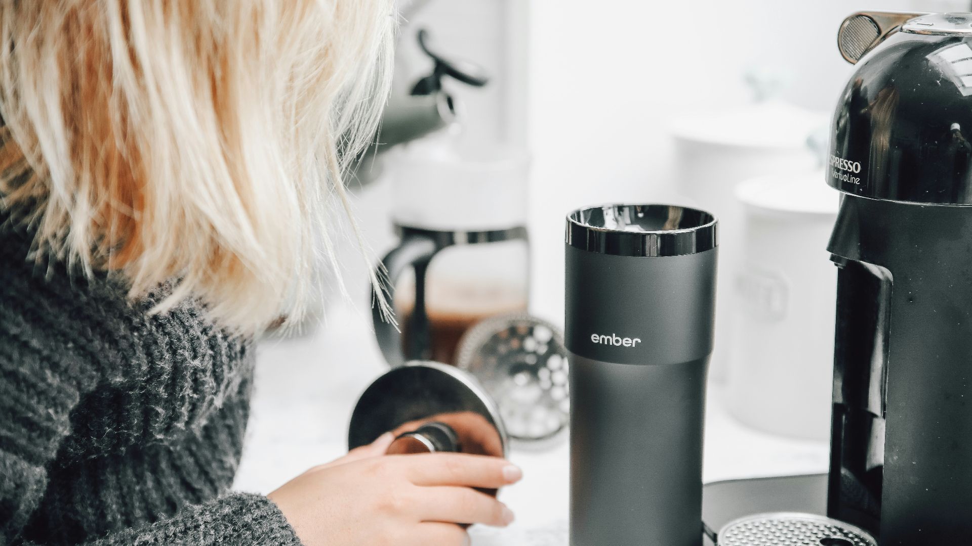 woman in gray sweater holding silver and black travel mug