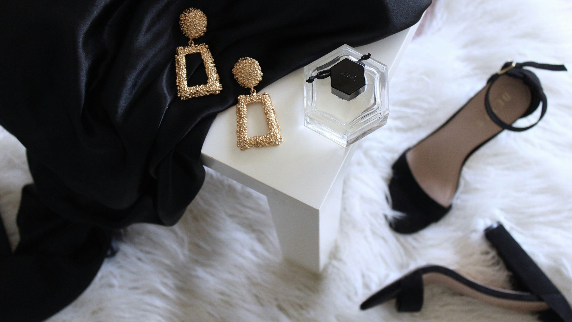pair of gold-colored earrings on table and black ankle-strap pumps on area rug