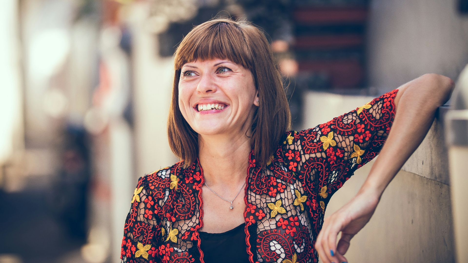 woman in floral-themed cardigan leaning on fence in bokeh photography
