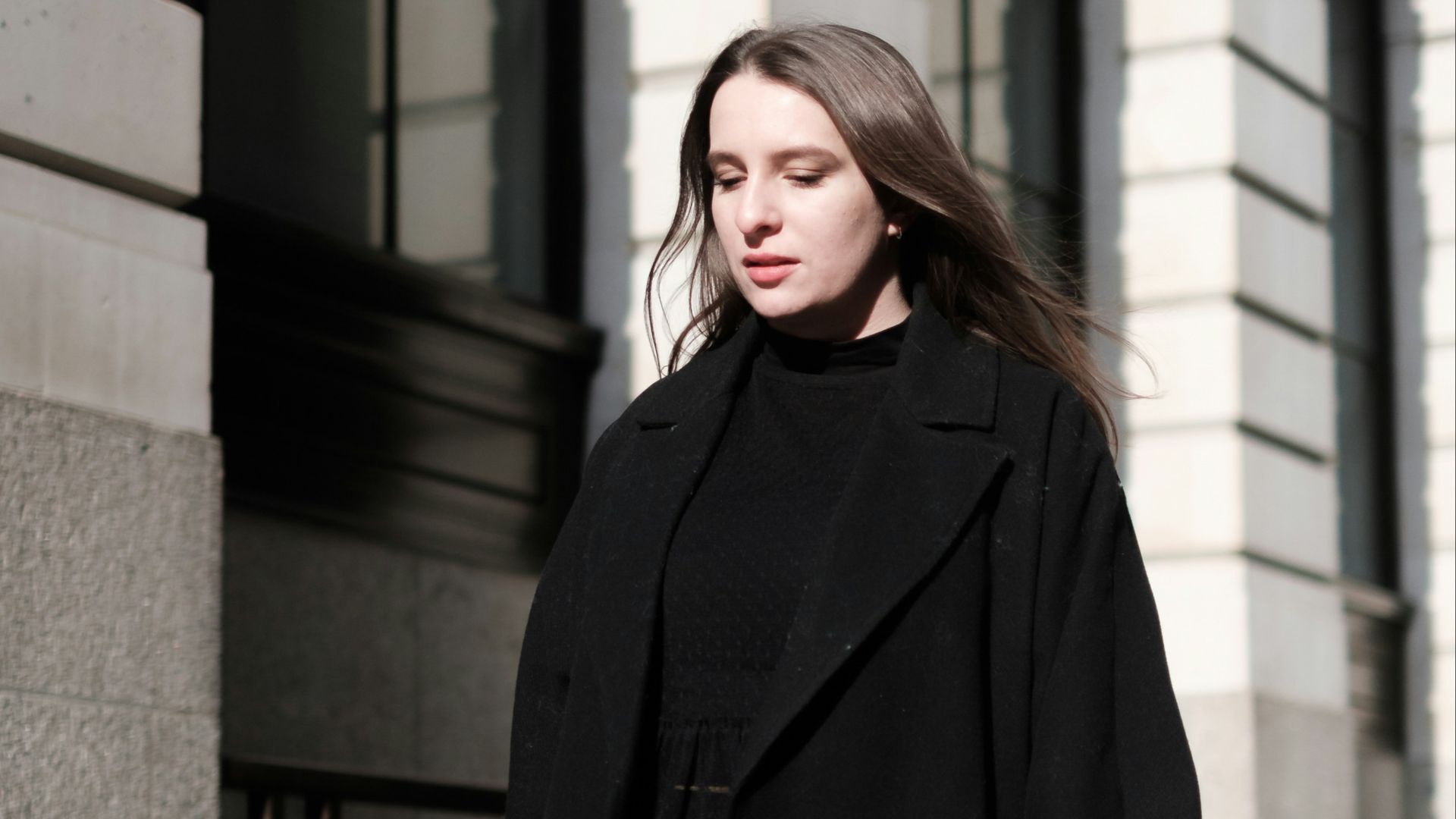 a woman in a black coat is walking down the street