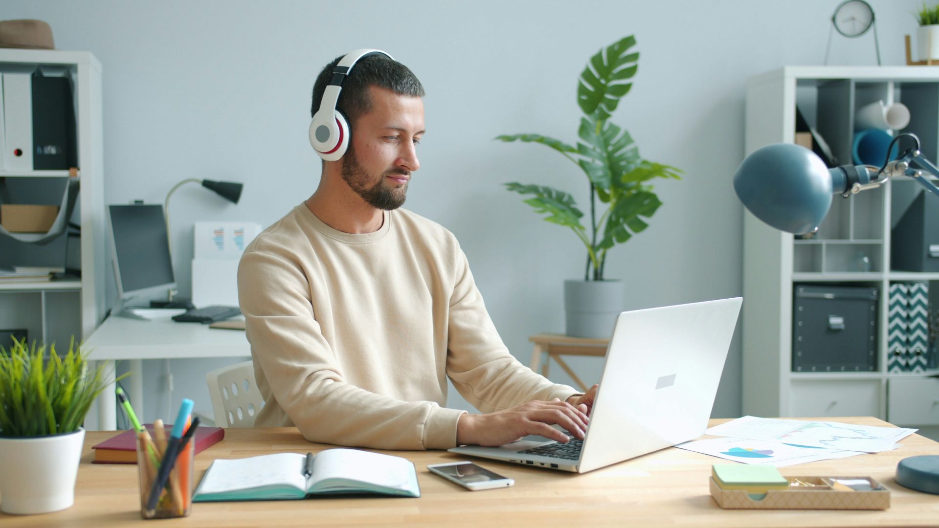 Man wearing headphones works on laptop at desk.