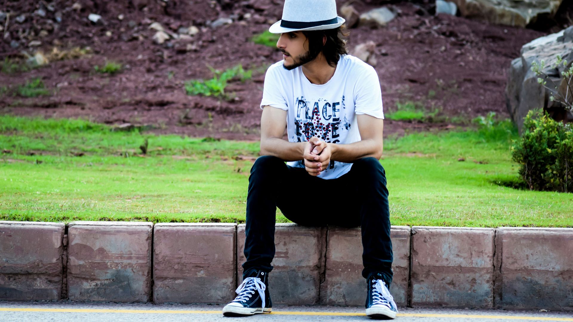 a man sitting on the side of a road wearing a hat