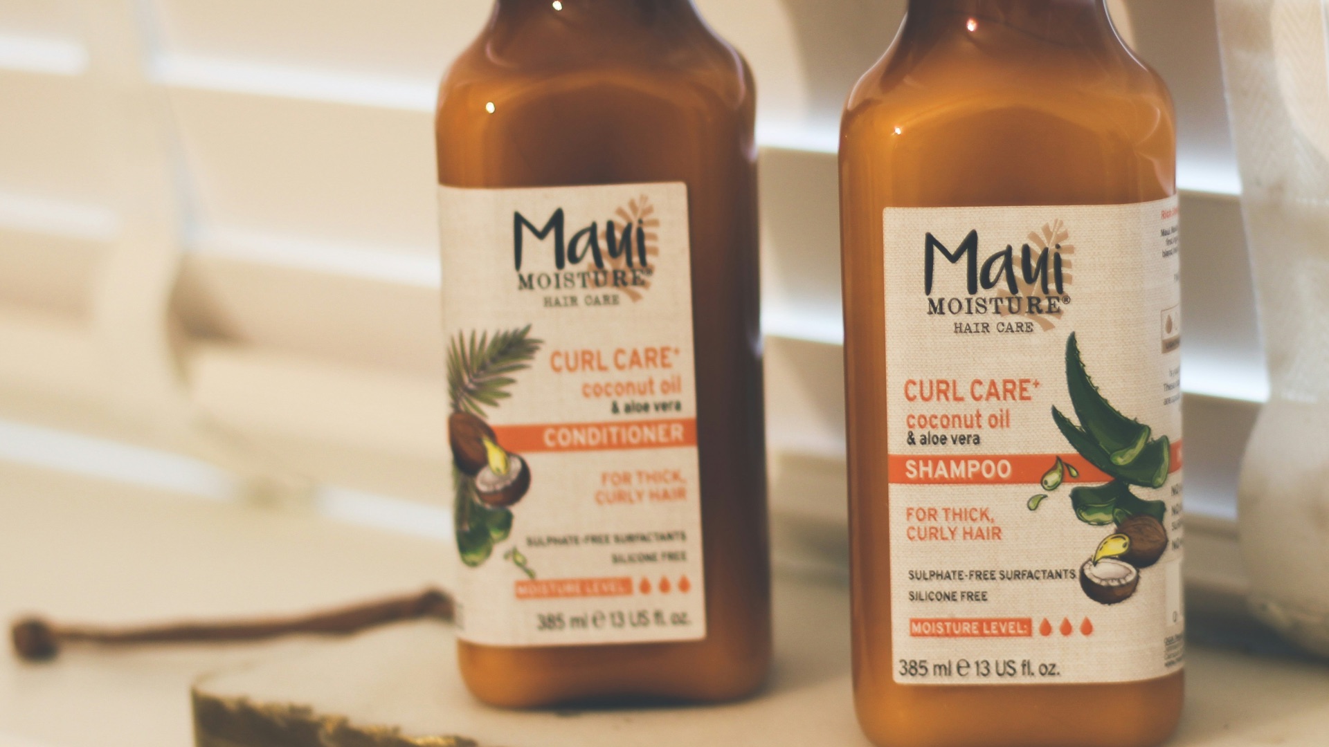 Two bottles of hot sauce sitting on a window sill