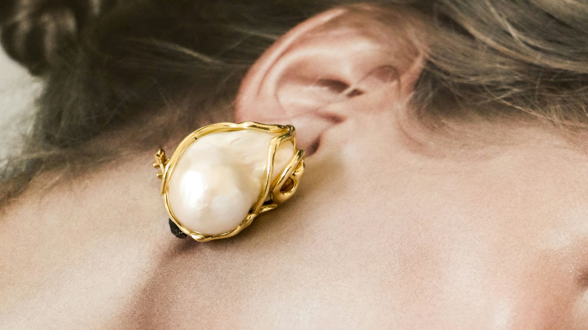 Elegant pearl and gold earring on woman's ear.