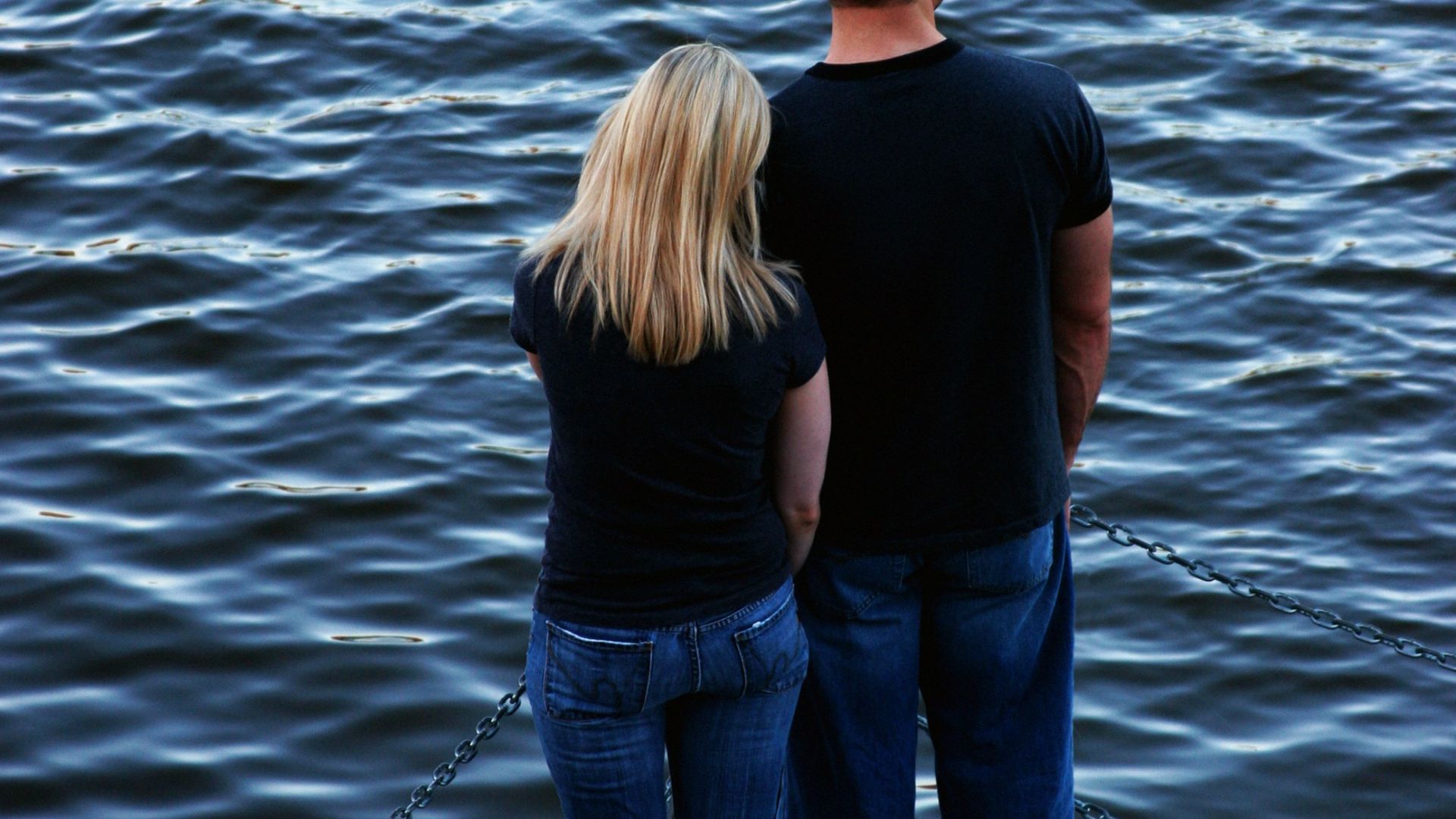 A man and a woman standing on a dock looking at the water