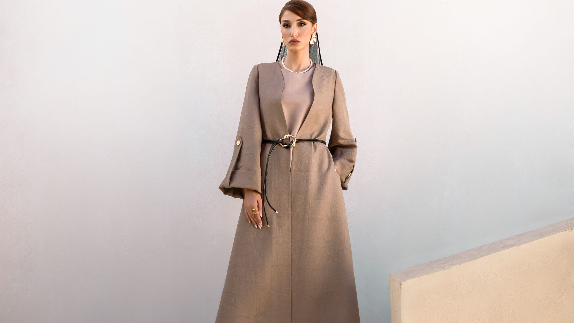 Woman in a long beige coat stands on stairs.