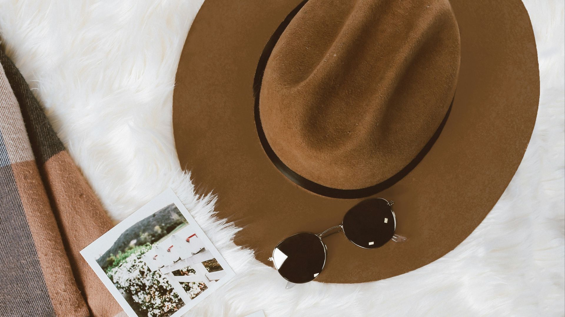 gold-colored framed sunglasses on brown hat beside white and black leather wristlet surrounded by photos on white and gray floral textile
