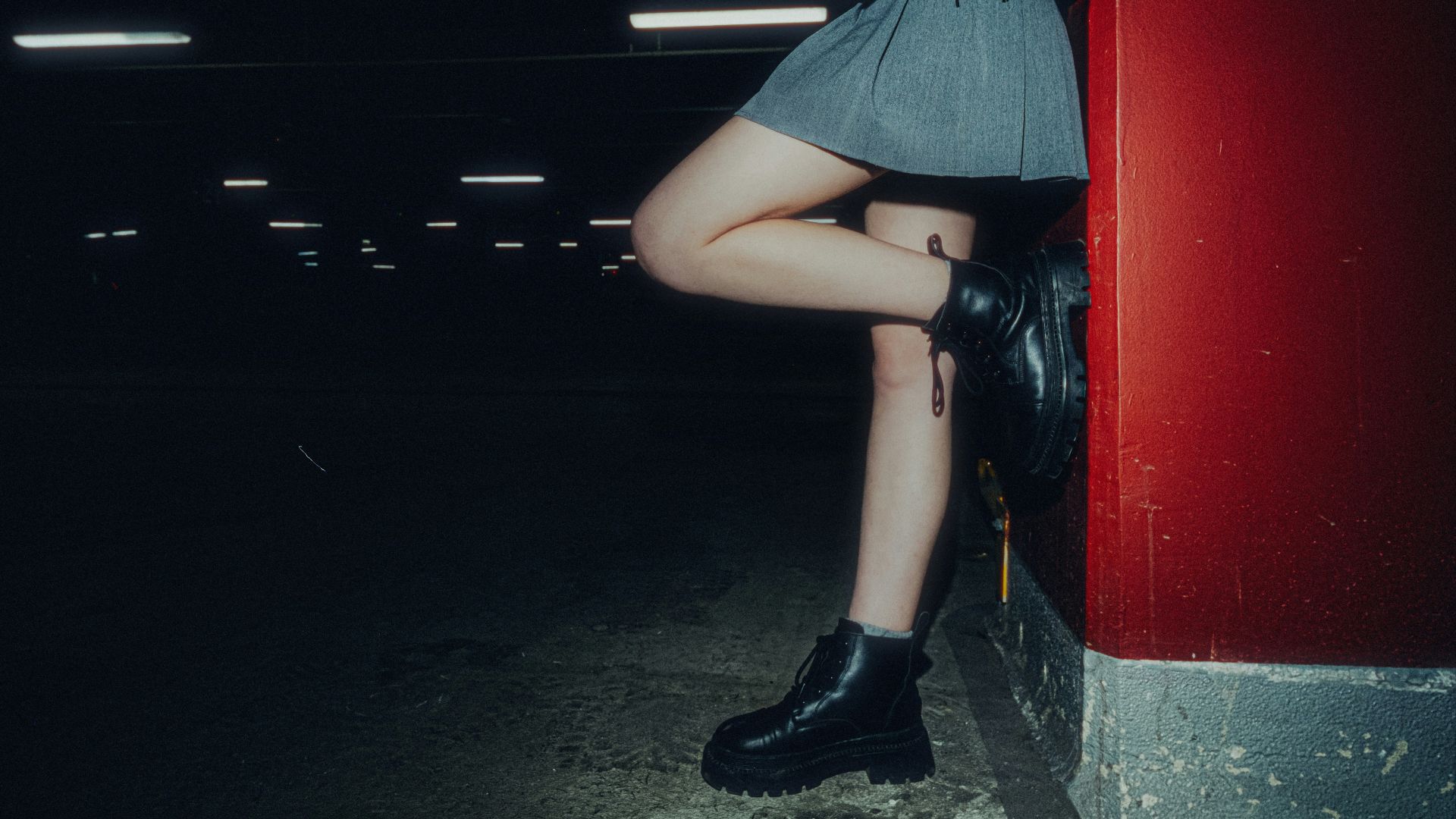 Woman in skirt and boots leaning against red wall