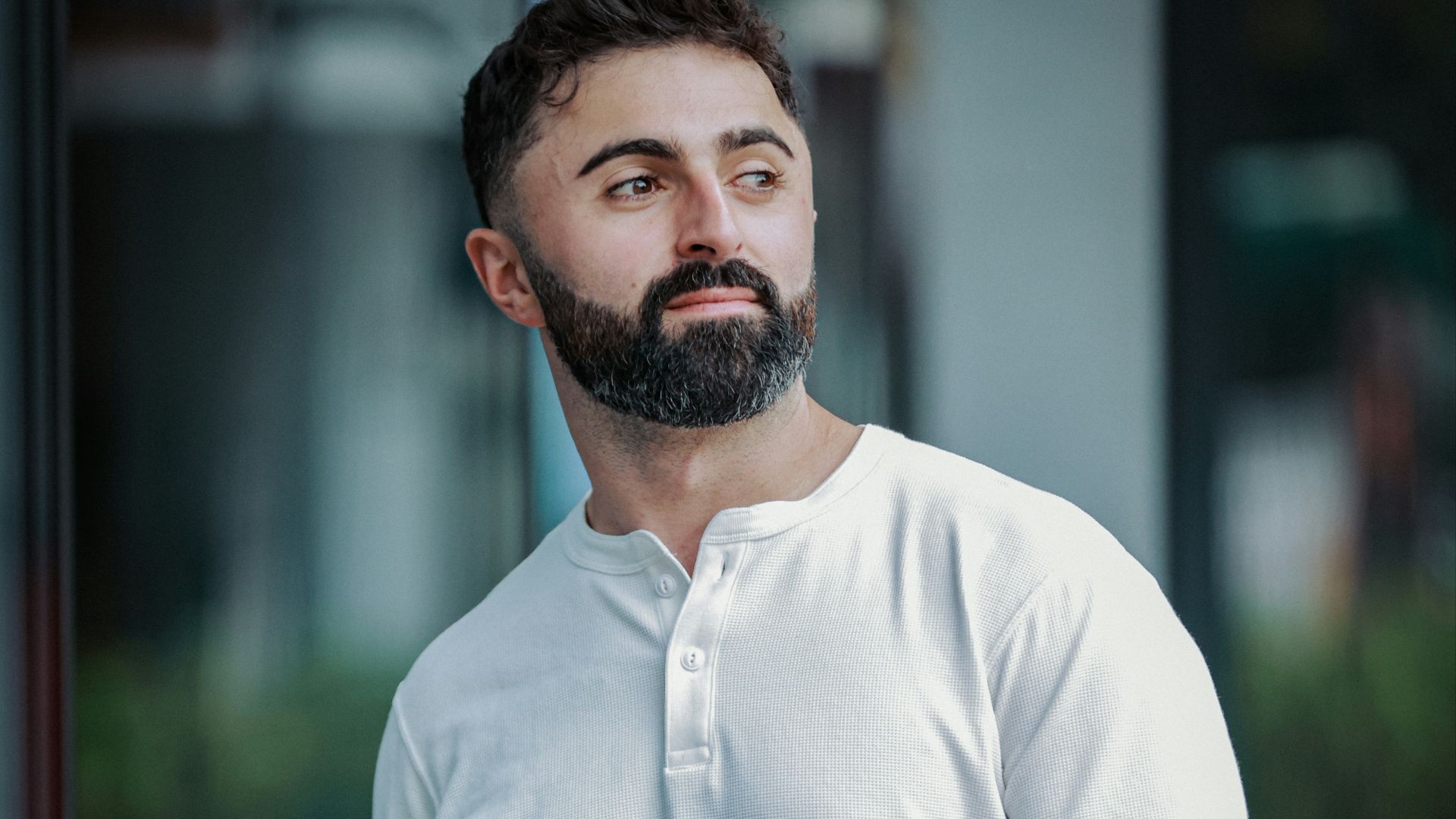 A man with a beard wearing a white henley shirt.