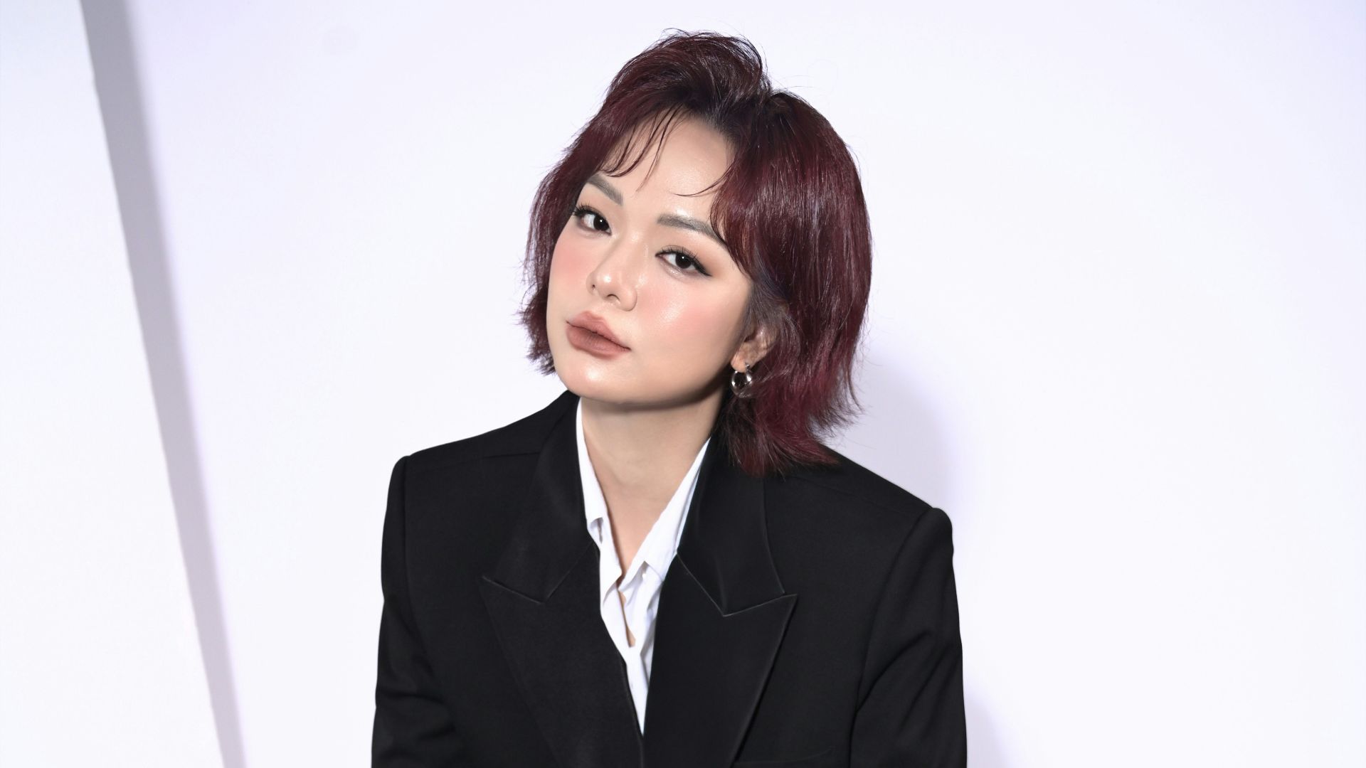 Young woman in black blazer sits on table.
