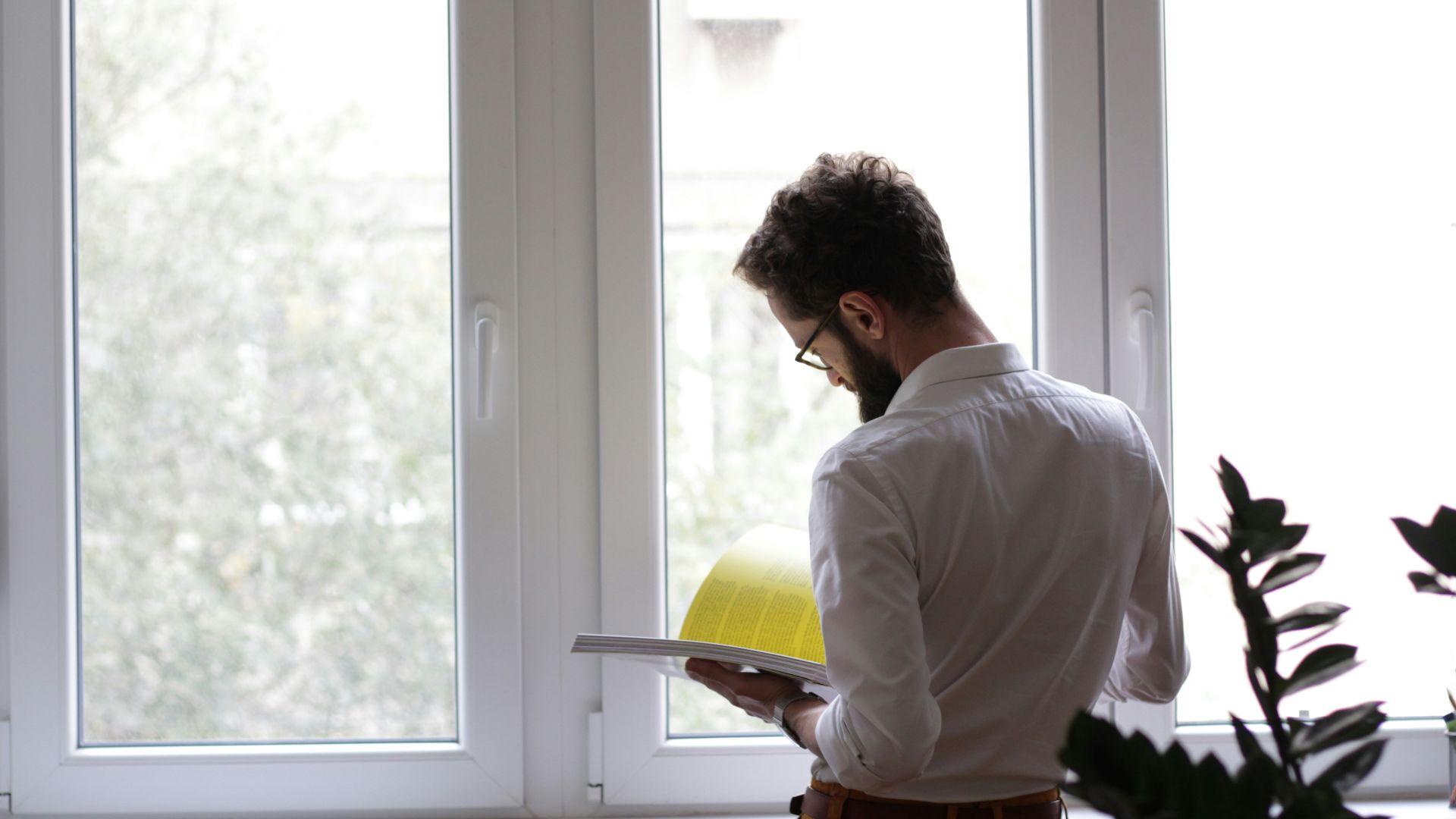 man reading book in front of window
