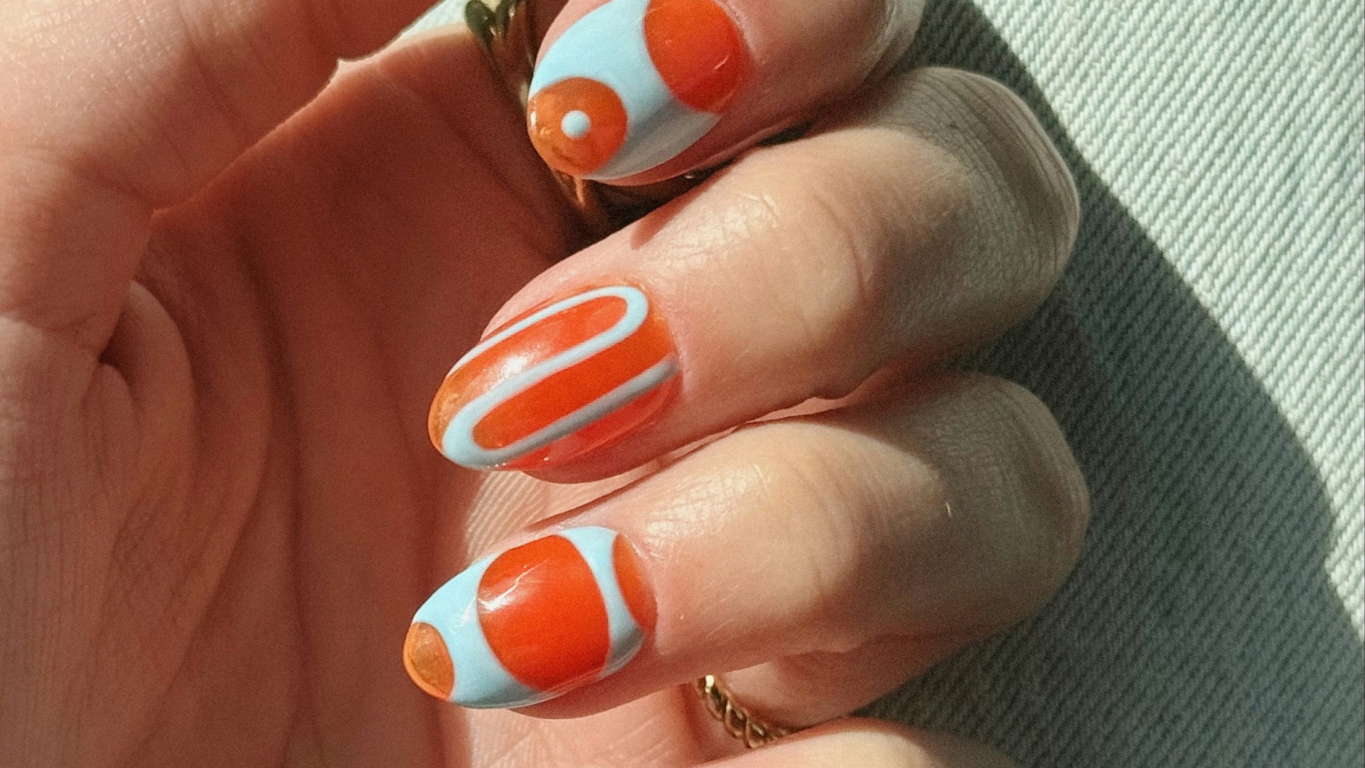 Hand with light blue and orange abstract patterned nails