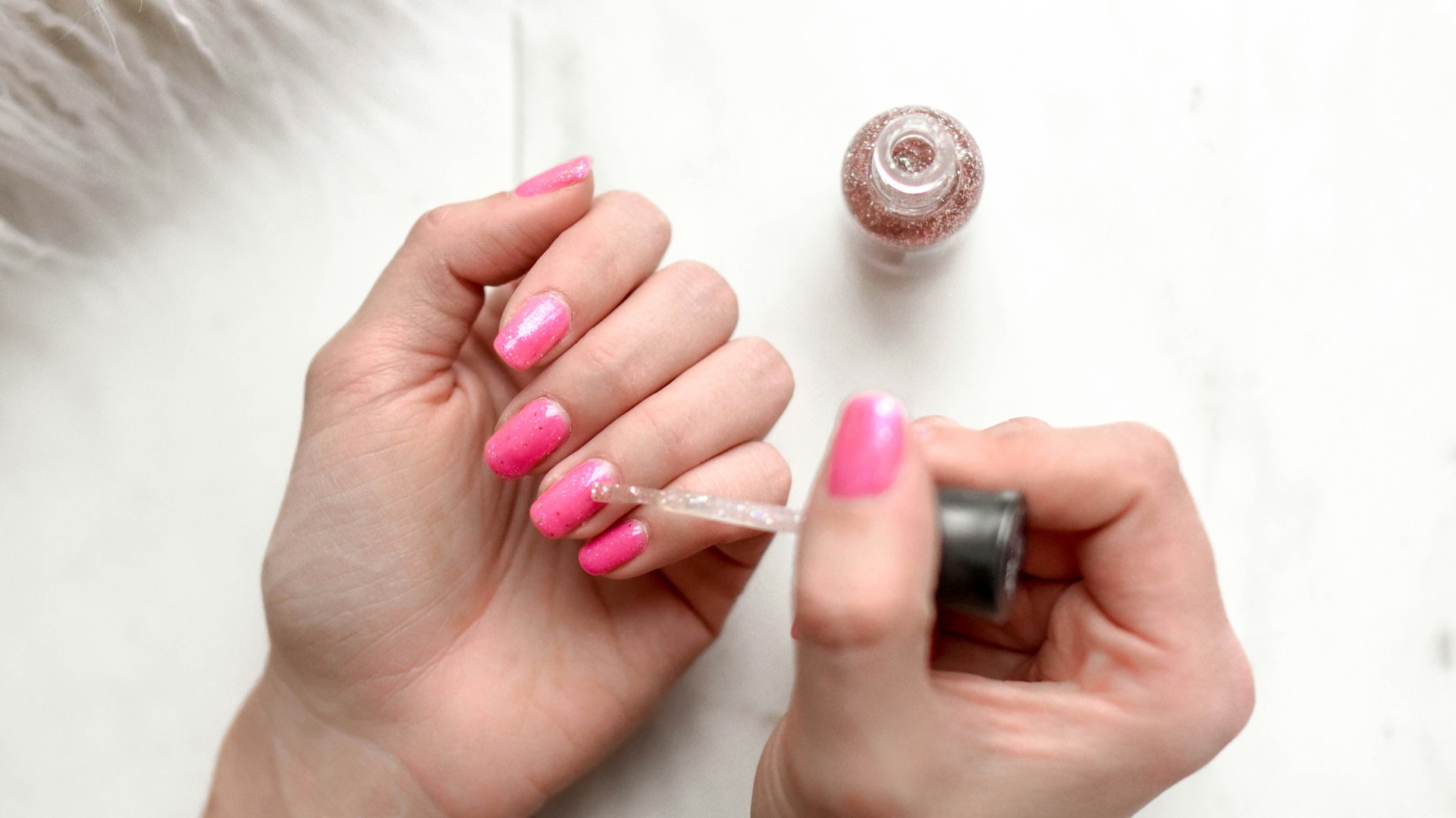 person spreading glittered nail polish on pink nails