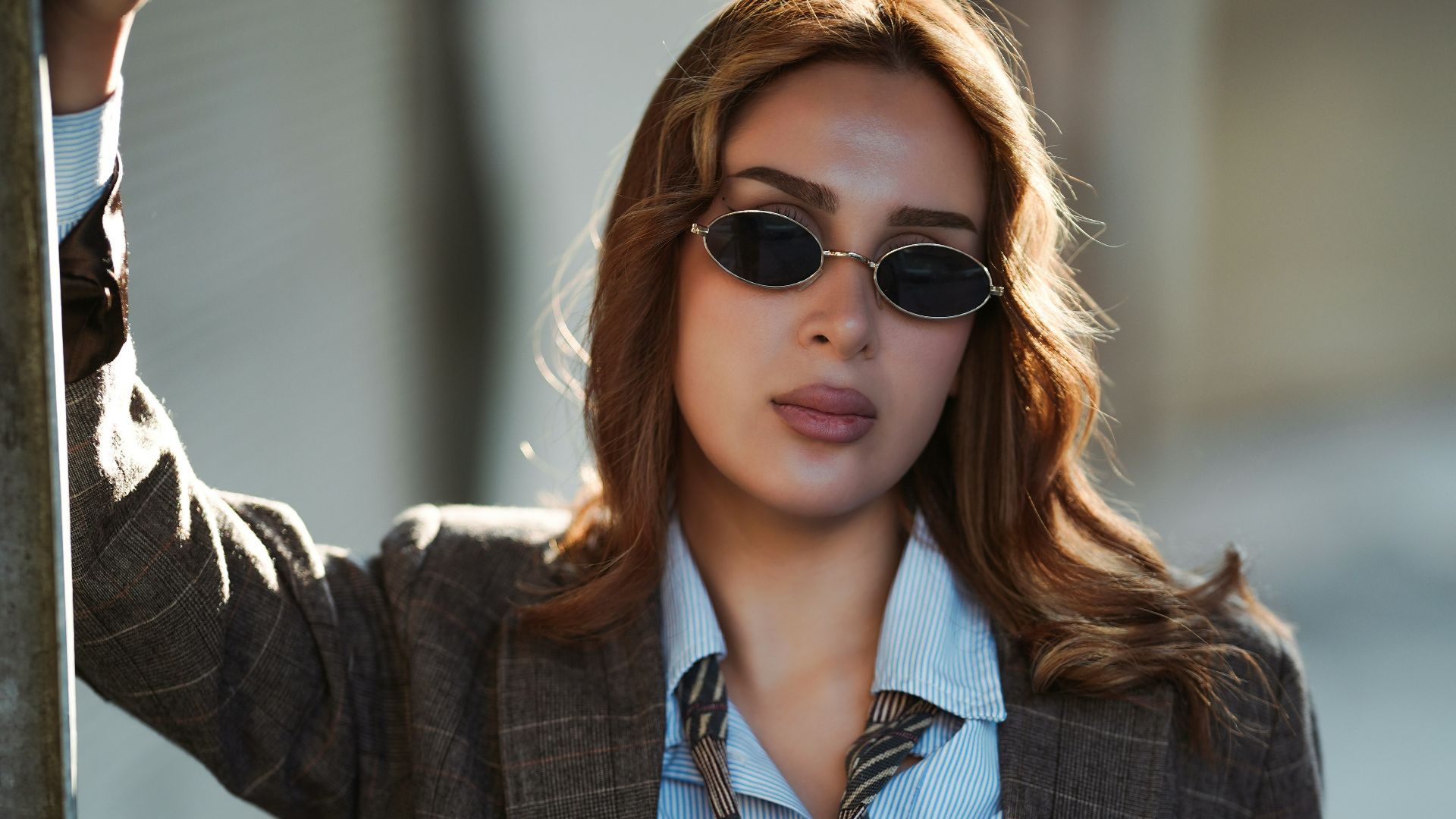 Woman in sunglasses and blazer leaning against railing.