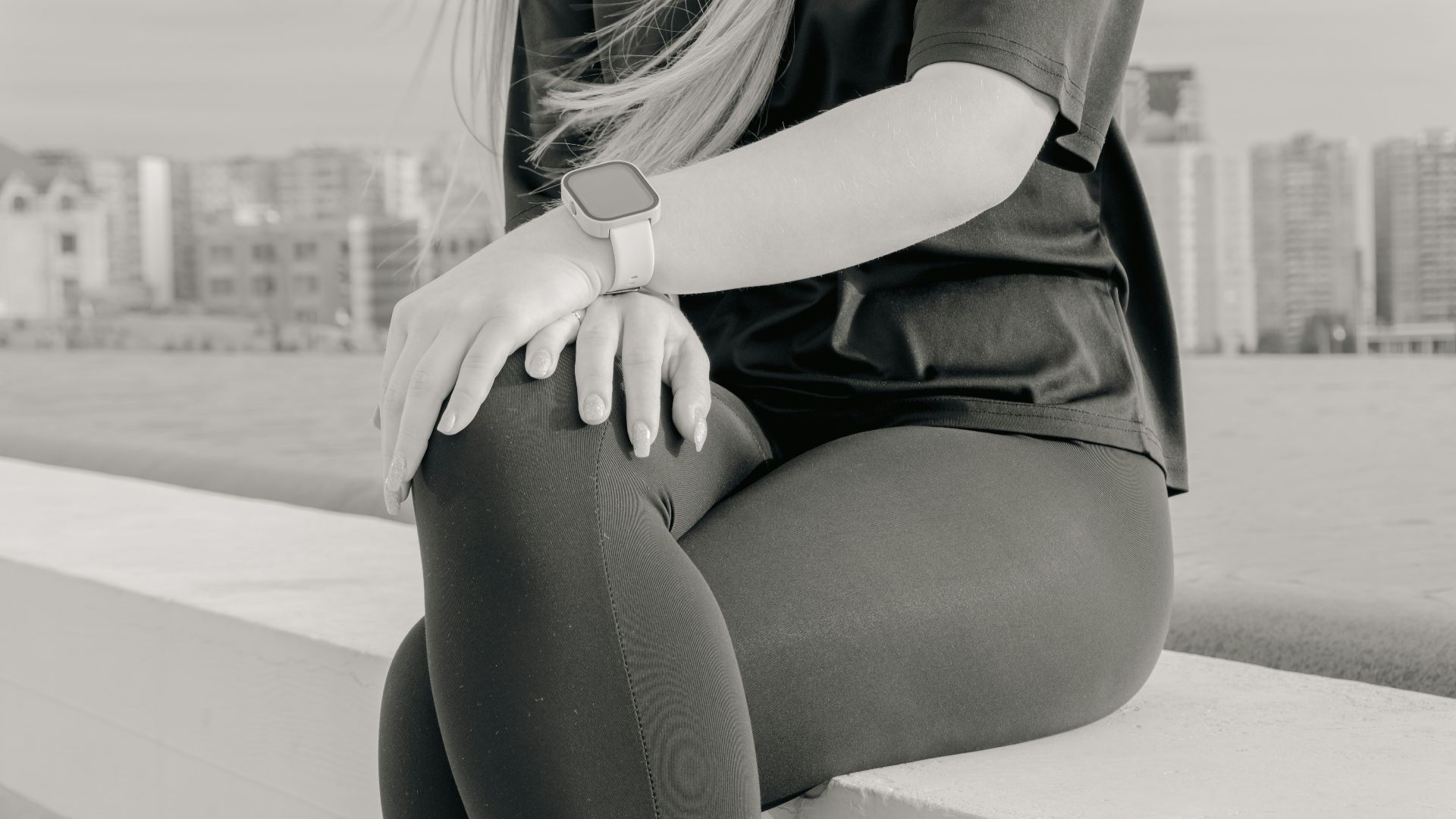 Woman in athletic wear sitting outdoors with city skyline.