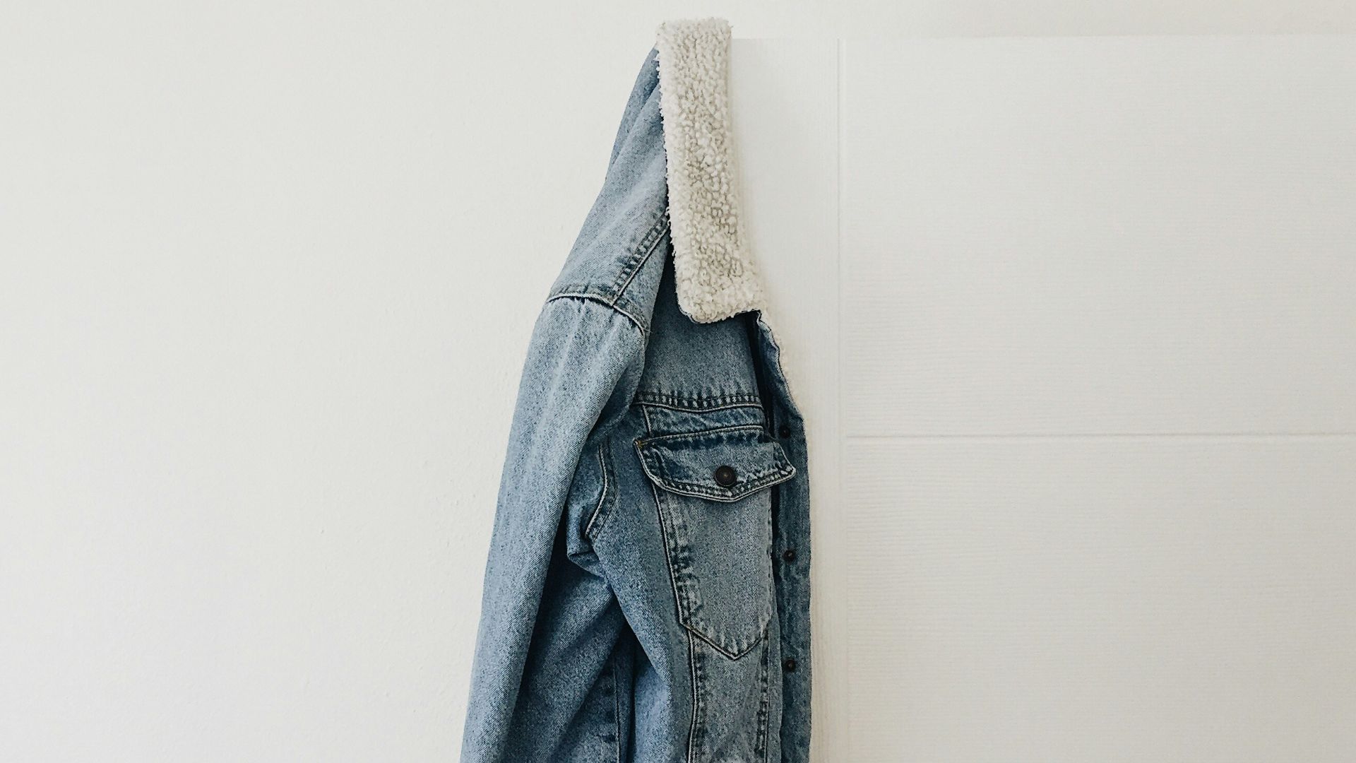 blue washed jacket hanging on white door