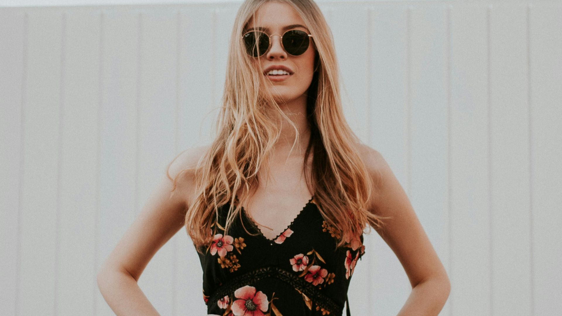 woman wearing black sunglasses standing near white wooden wall