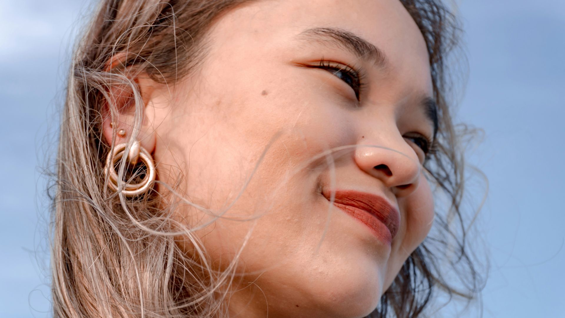 Young woman with blonde hair and hoop earrings smiles.