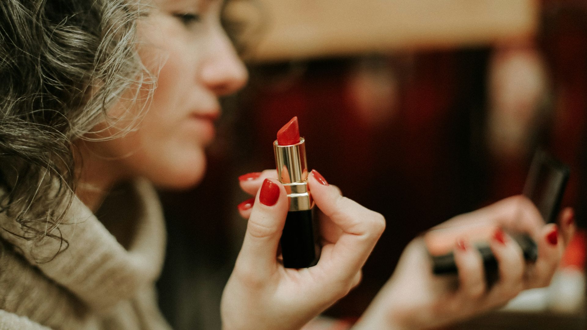 woman in gray sweater holding lipstick