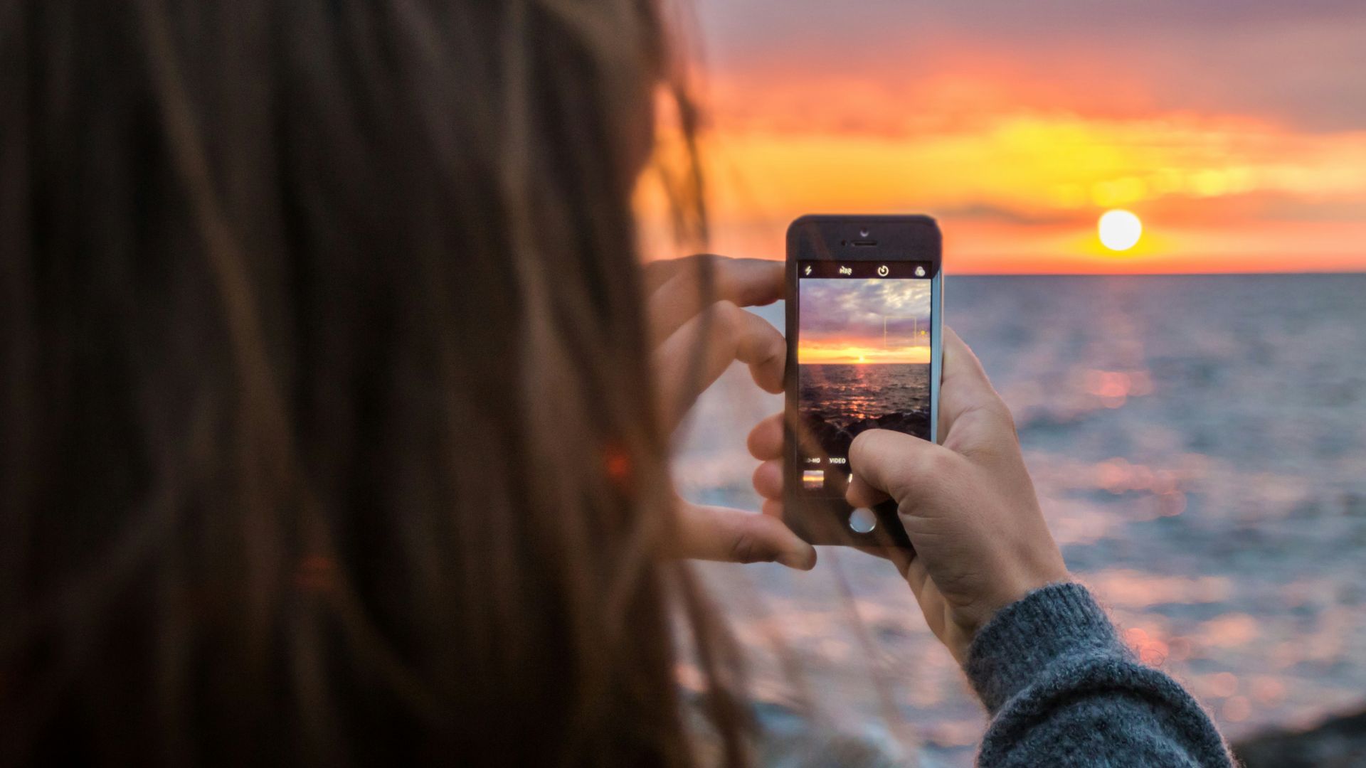 woman holding phone taking a photo of sunset